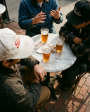 Friends in Paulie's Original Caps sharing drinks at a sidewalk cafe table