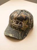 Paulie's Camo Cap, a tree camo snapback hat with the cream embroidered Paulie's oval logo