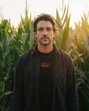 Man wearing the black Paulie's Oval Tee standing in a cornfield